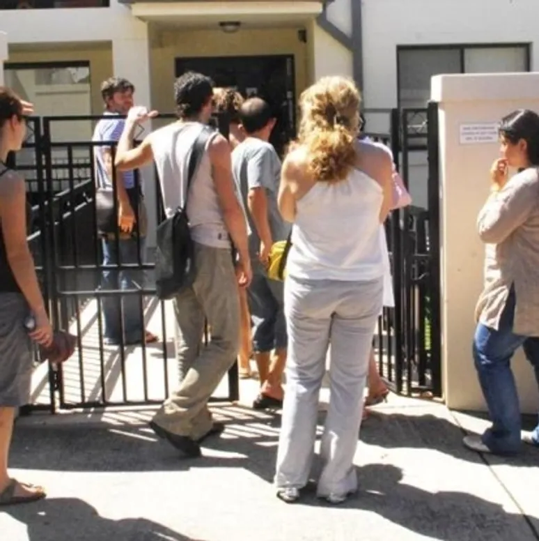 A number of people in casual clothes wait around the front door of a property, presumably to inspect it before applying to rent it.