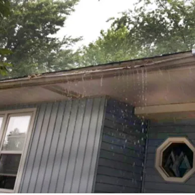 Rain falling down from a house's gutter. The guttering doesn't seem well maintained.